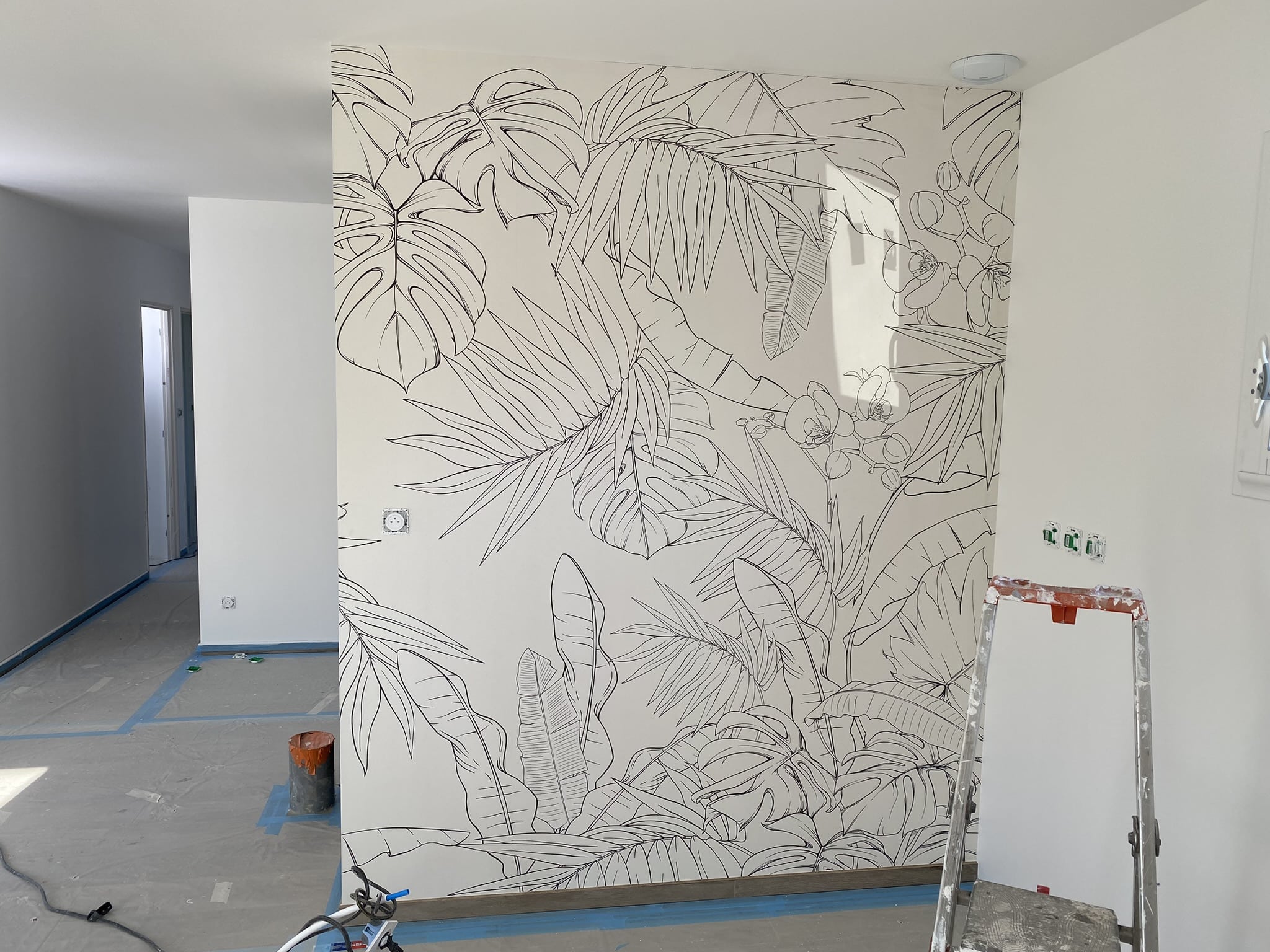Fresque murale botanique au trait noir pour intérieur Fresque murale tropicale en traits noirs sur mur blanc dans une pièce en cours de rénovation avec échelle de chantier.